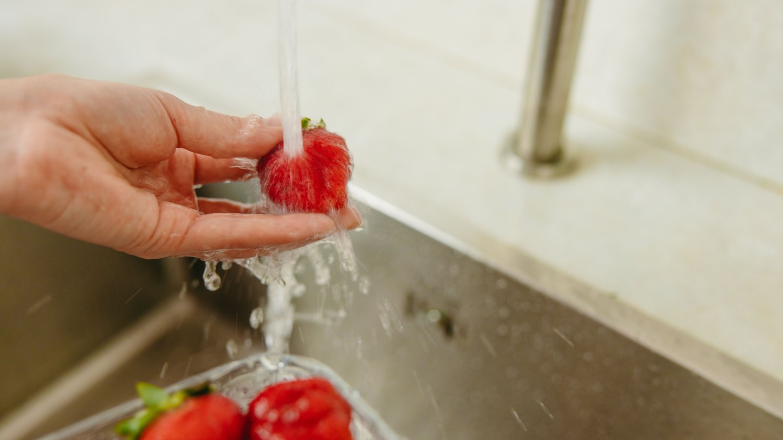 A hand washes strawberries under running tap water, not a photograph of these advisories.
