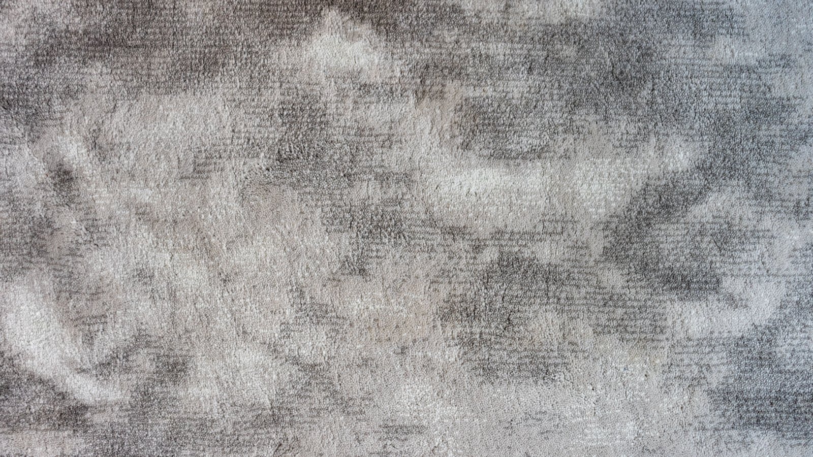 A close photograph of a dense grey and cream pile surface filling the whole frame, its fine vertical nap broken by soft darker and paler cloudy patches. No text, markings, people or objects are in view.