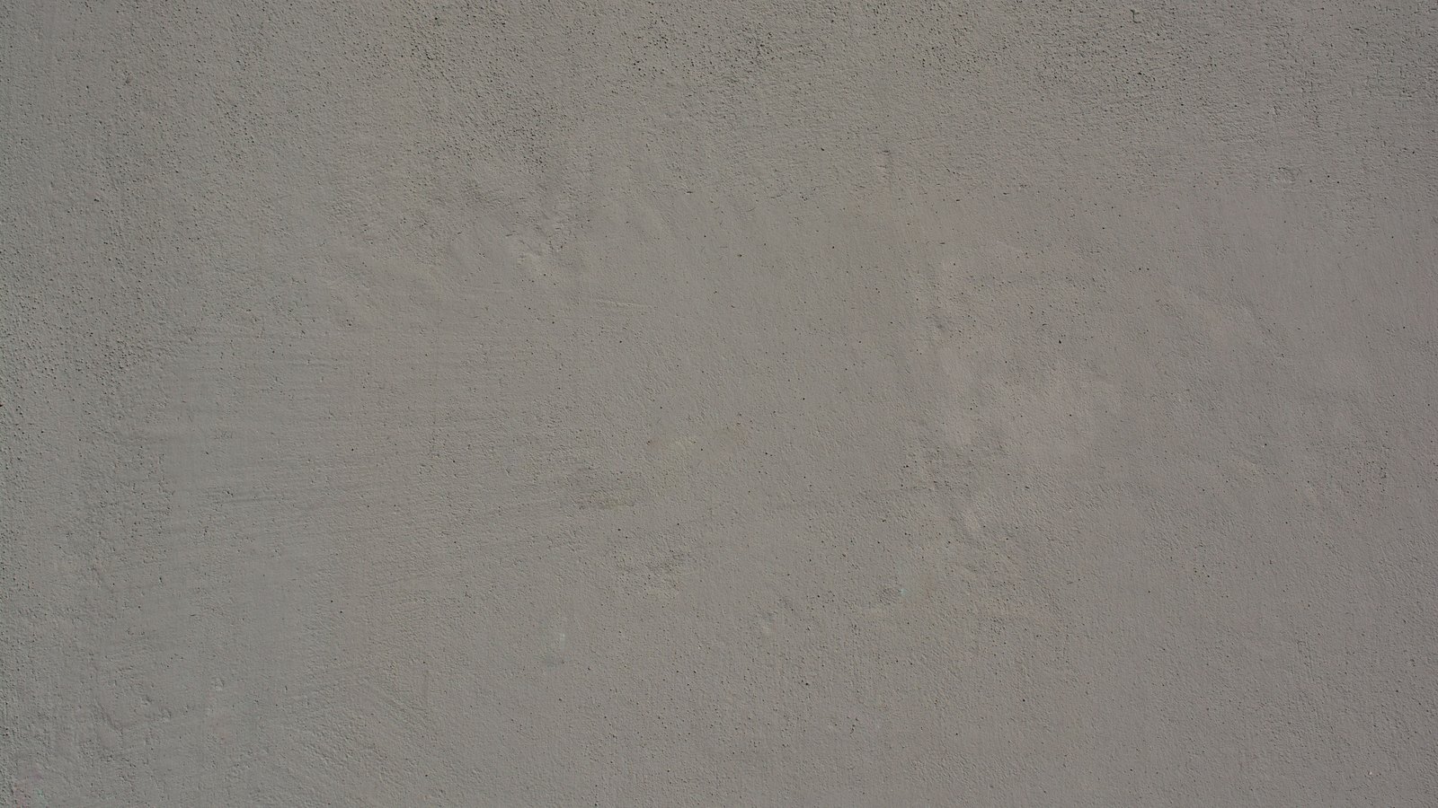 A flat, evenly lit close crop of a plain grey rendered surface, filling the whole frame, showing nothing but a faint mottling in the render and a scattering of small dark pores in it. There is no text, signage, lettering, brand mark, person, vehicle, machine, structure or identifiable place anywhere in the frame. This is a blank texture used deliberately as a placeholder rather than a picture of anything: it is not a photograph of the Cape Coral gas leak, of the excavator, of the struck line or of the evacuated blocks, and the Pexels library records it as a grey wall rather than the ground surface the search asked for. Its weakness is that it depicts nothing at all, which was preferred to the alternatives the search actually returned, every one of which would have depicted the wrong thing: a warning sign carrying a different gas company's name and emergency number, a wheel loader in a sand quarry, and a residential street in Germany.