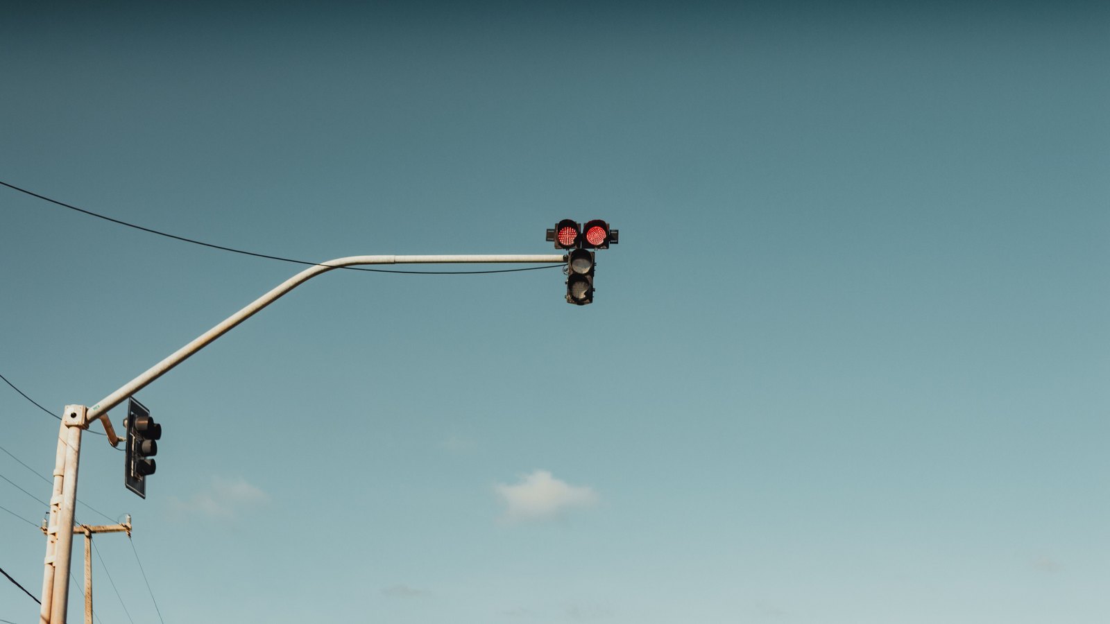 A traffic signal head hanging from a curved metal mast arm against a plain blue evening sky, two red lamps lit, with overhead power lines and the top of a wooden utility pole at the lower left. No road, vehicle, person, building, signage or lettering of any kind is visible in the frame. Stock photograph, not a photograph of this event.