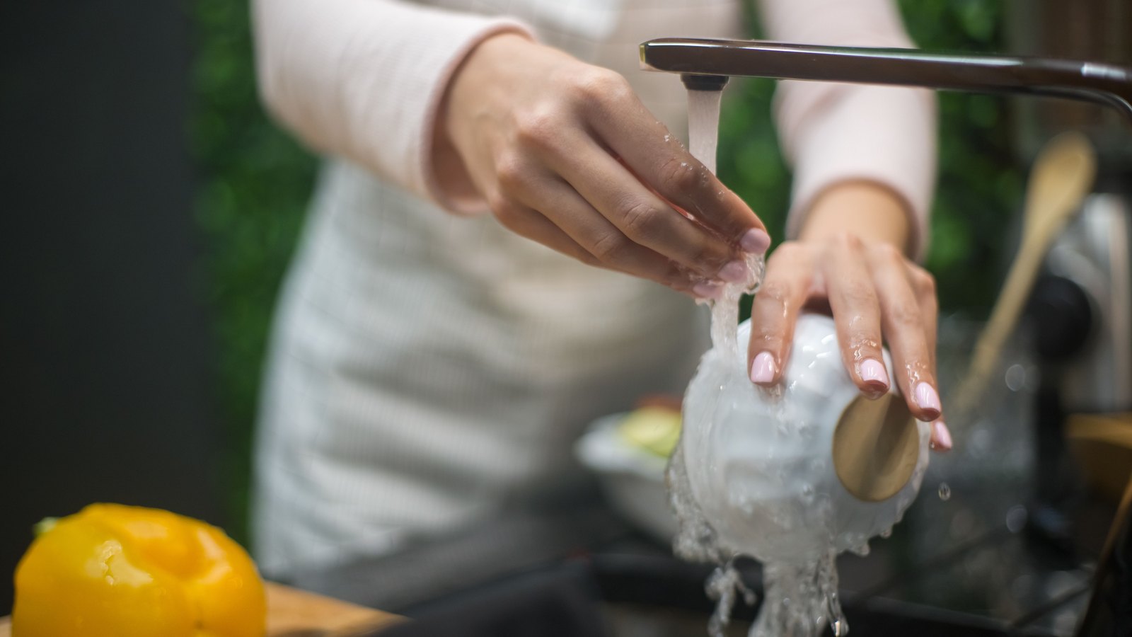 Hands washing a white bowl under a running kitchen faucet, with the person cropped below the face and no legible text. A stock photograph, not a photograph of this event.