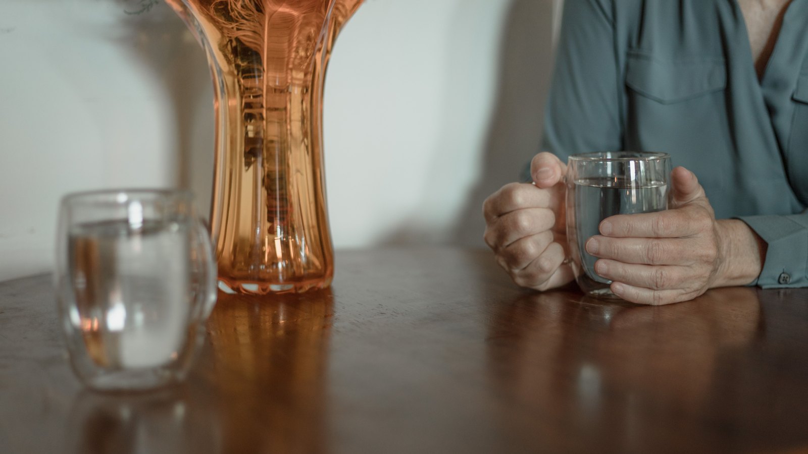 Hands hold a glass of water beside another glass and an amber pitcher, not a photograph of this event.