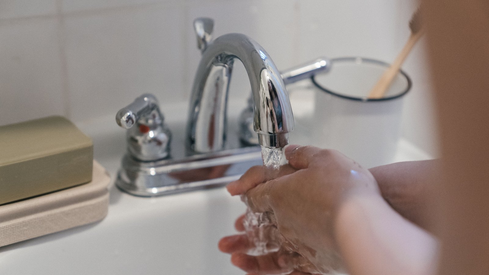 Hands being washed under a running chrome faucet, with no face or legible text visible. A stock photograph, not a photograph of this event.