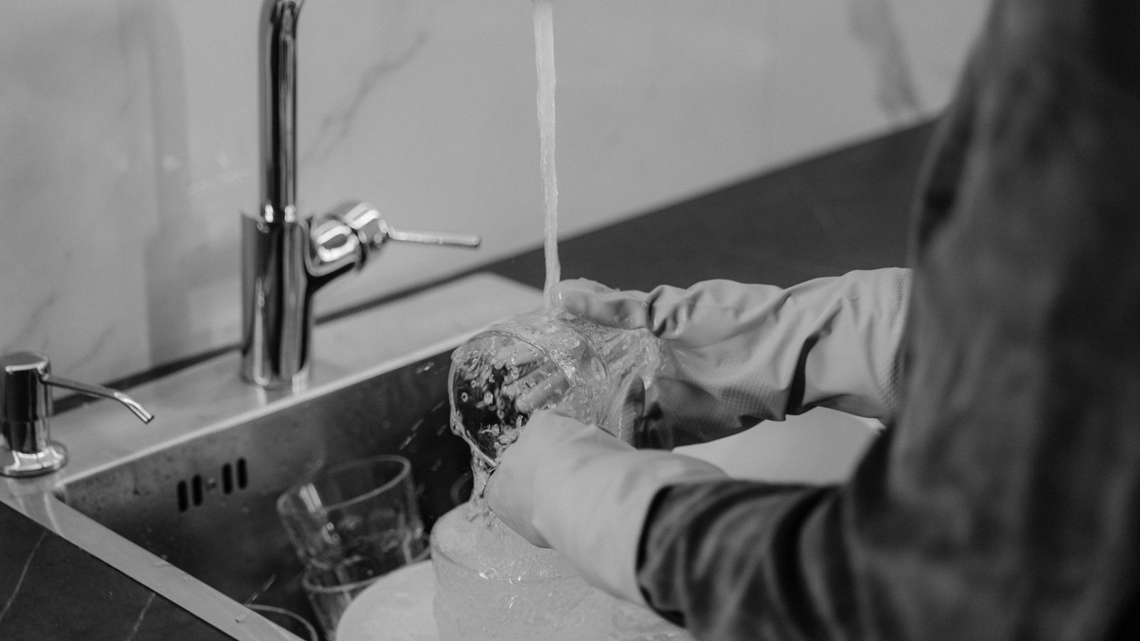 Gloved hands washing a glass under a running kitchen faucet, not a photograph of this event.