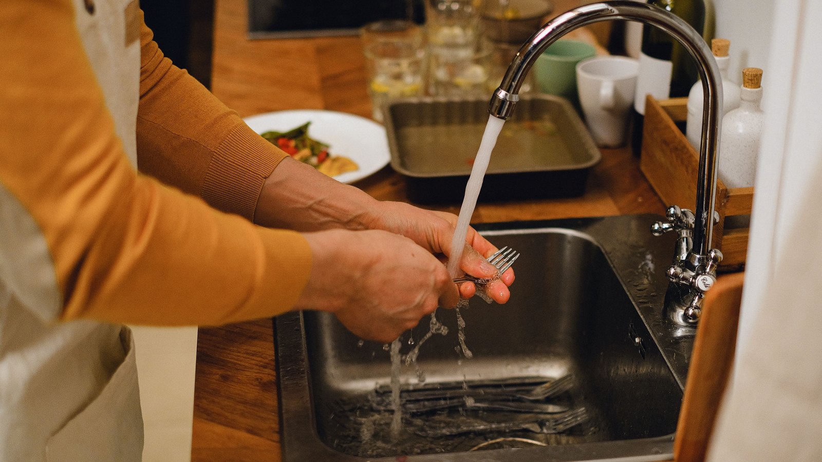 Hands washing a fork beneath a running kitchen faucet, not a photograph of this event.