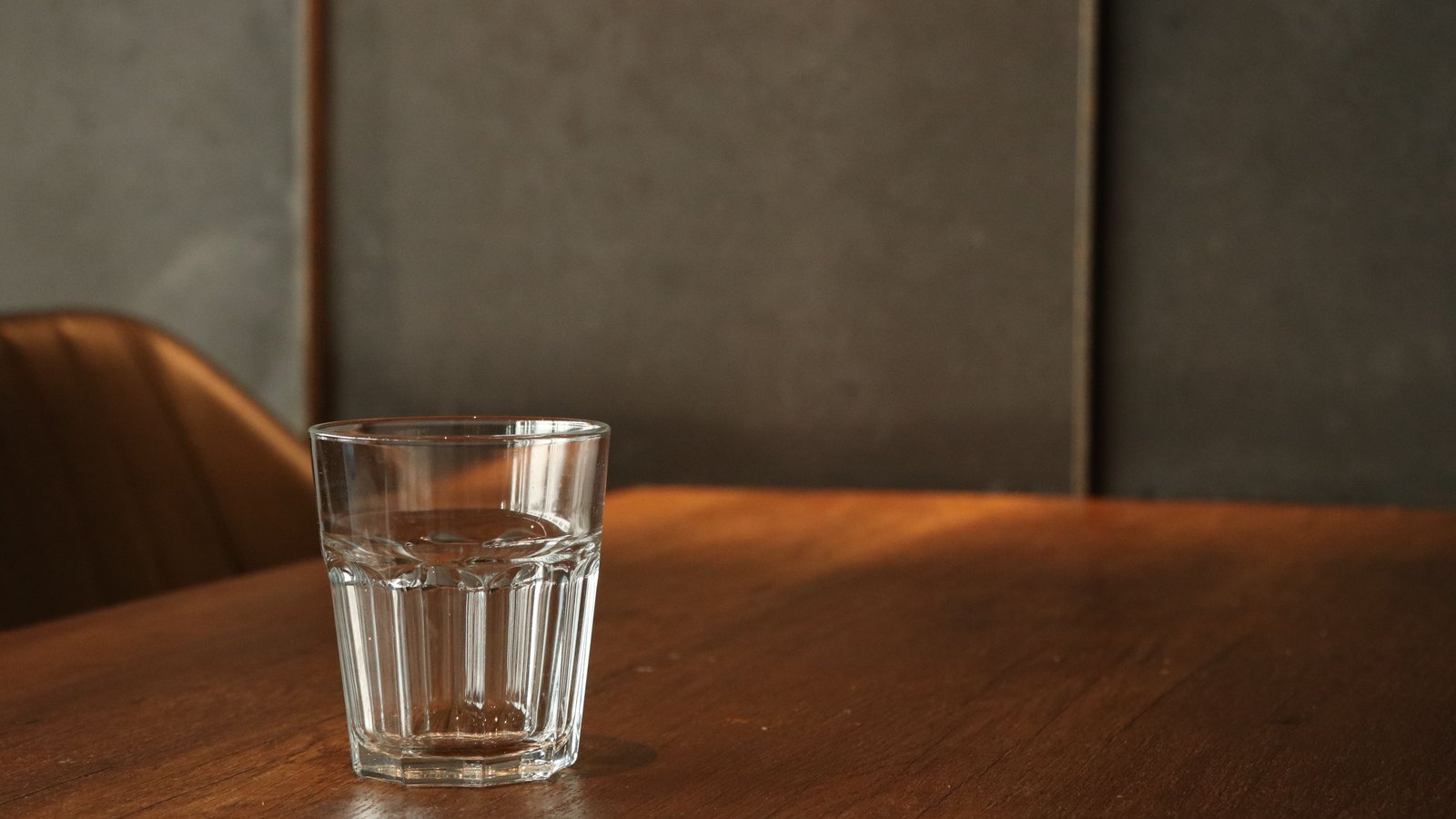 A clear glass of water rests on a wooden table in warm indoor light, with no person, text or identifiable location visible. A stock photograph, not a photograph of this notice.