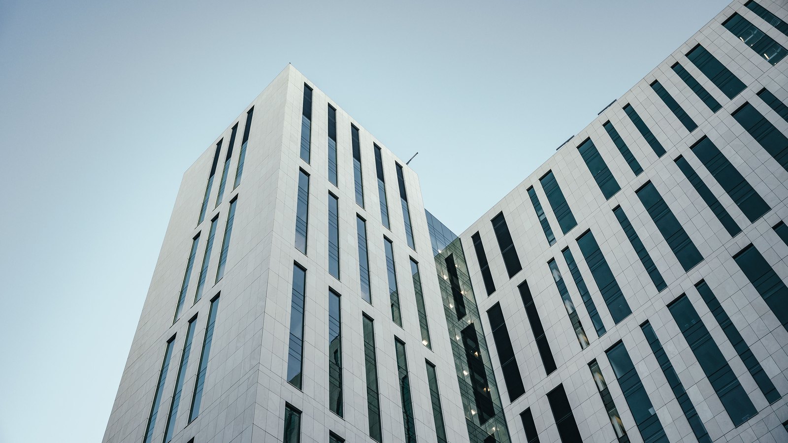 The upper storeys of two modern office towers in pale stone and glass, seen from below against a clear sky. No signage or logo appears. A generic illustration of a corporation, not a photograph of any company in this story.