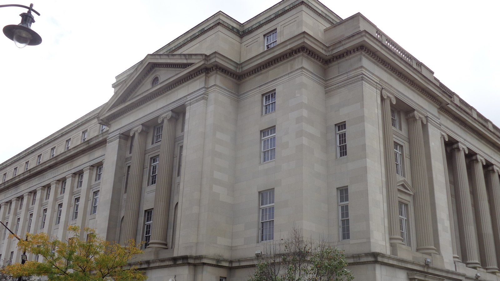 The corner of the United States Post Office and Courthouse on Federal Square in Newark, a pale limestone building with ionic columns running along two elevations under a plain pediment, photographed from the pavement against a white sky.