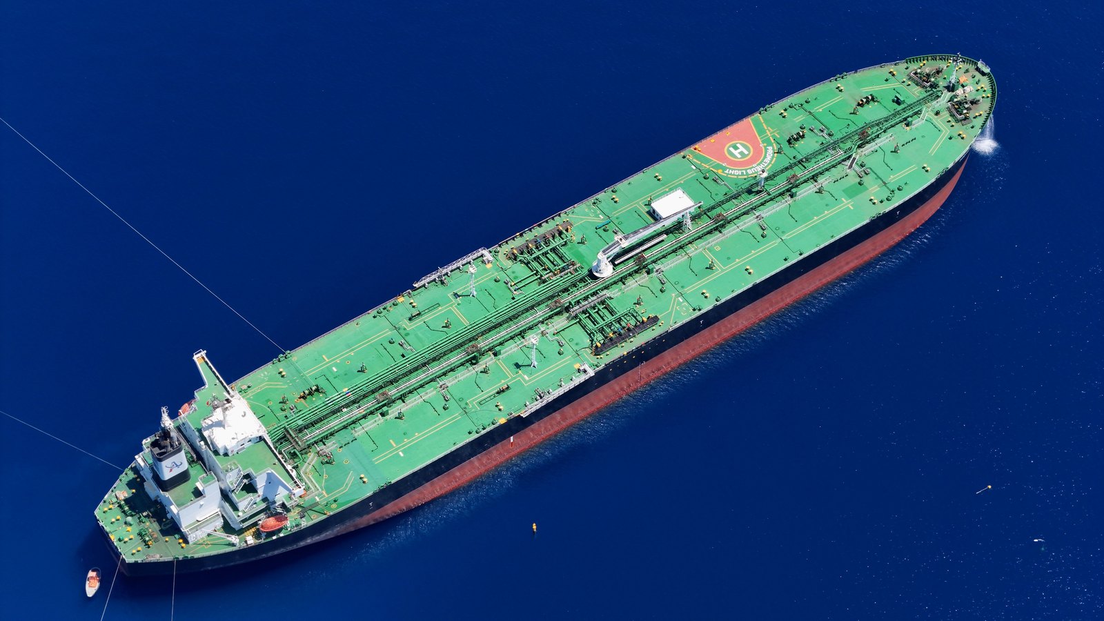 Aerial view of a laden crude oil tanker with a green deck and red hull under way on open deep-blue water.
