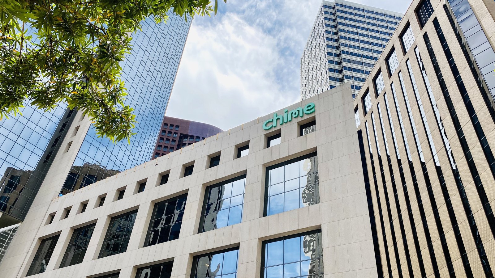 The Chime Financial headquarters in San Francisco, its teal logo mounted above a pale stone facade between glass office towers.