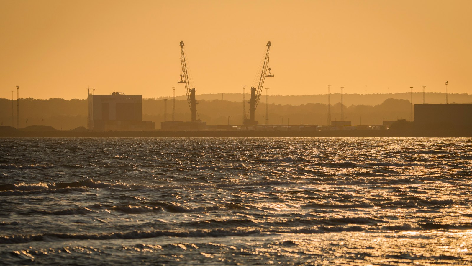 Two harbor cranes silhouetted across choppy water at sunset