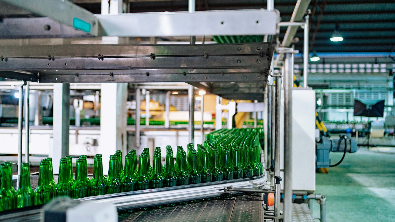 Rows of green glass bottles move through an automated factory conveyor.