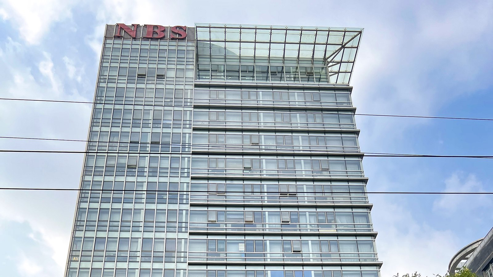 The glass facade of China's National Bureau of Statistics, with red NBS letters above the roof.