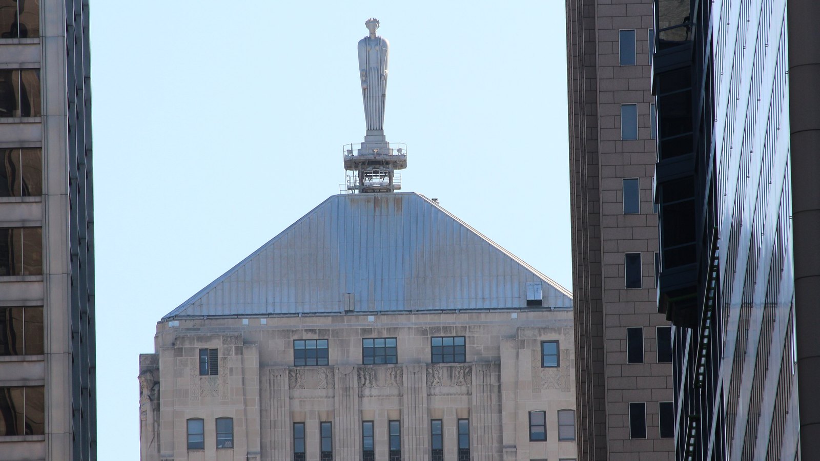 The pyramidal metal roof of the Chicago Board of Trade Building topped by its stylised statue of Ceres, framed between two neighbouring towers against a pale sky.