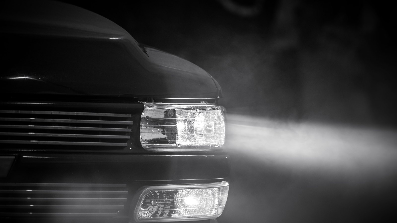 A tight black and white crop of car headlights shining through mist, with no person, plate, logo, sign or identifiable place, not a photograph of this event.