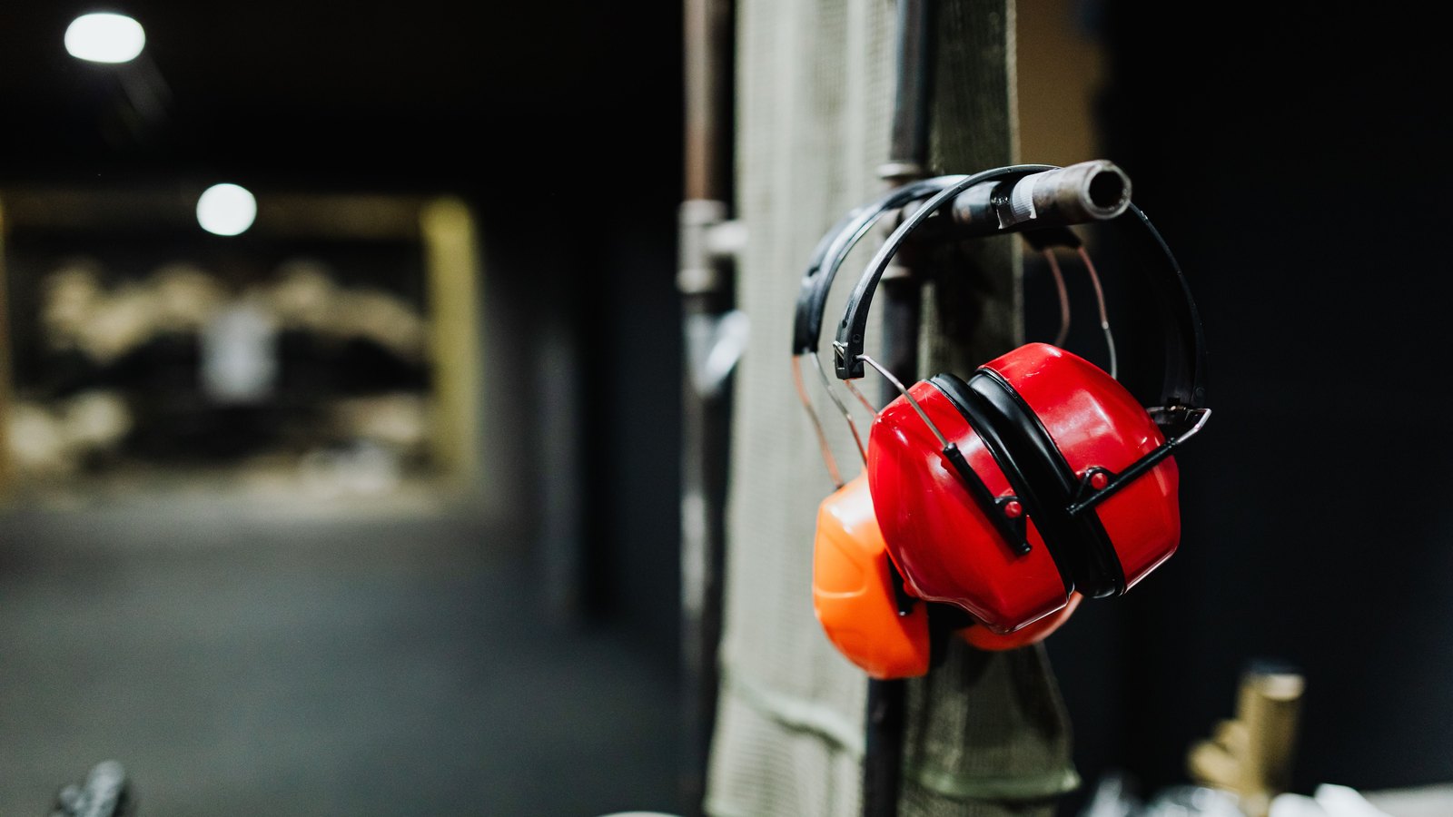 Red hearing protectors hang beside an indoor shooting lane, not a photograph of this event.