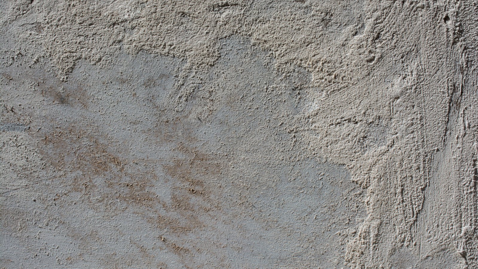 A close crop of a plain grey rendered concrete surface, its finish uneven and streaked with pale sandy patches. No people, vehicles, roads, markings, signage or lettering are visible and no place can be identified from it. An abstract surface used as a plain illustration, not a photograph of Davis Boulevard, of Naples or of this crash.