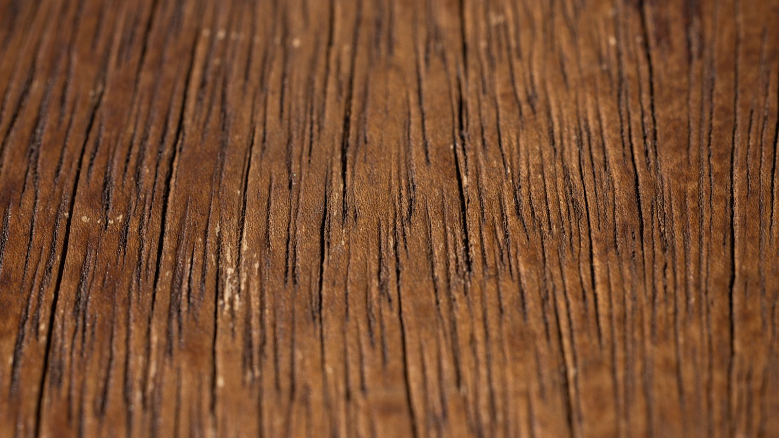 A close macro of brown wood grain filling the frame, the open grain lines running vertically and lightening towards the top.