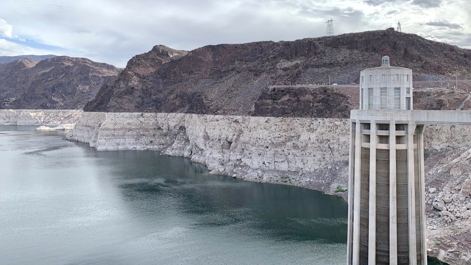 One of the concrete water intake towers standing in Lake Mead at Hoover Dam, with a wide band of bleached white rock running along the shoreline behind it above the present water line.