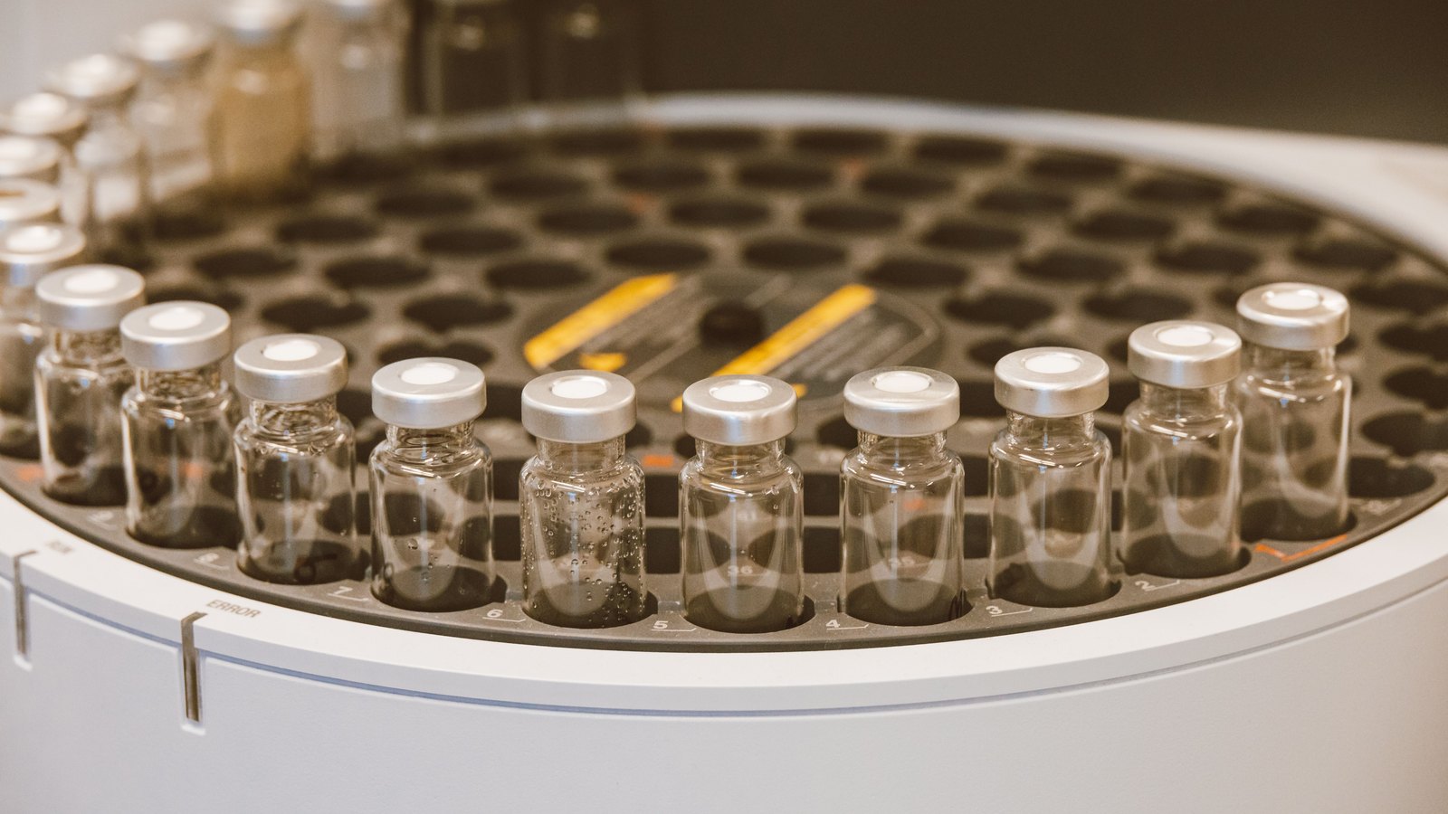 Unlabeled glass vials in a laboratory carousel, not a photograph of the medicines covered by the tariff notice.