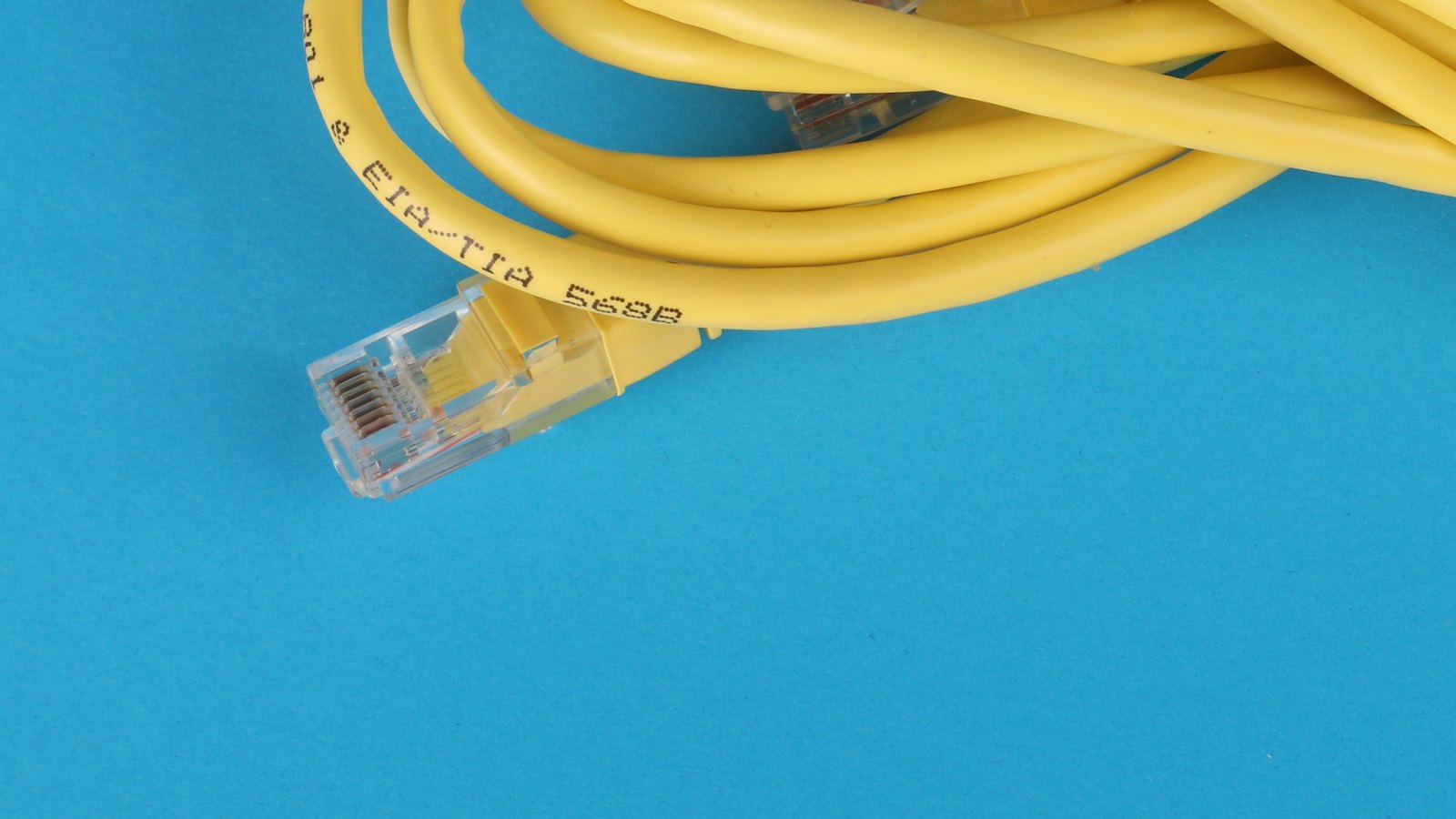 A clear Ethernet plug and yellow network cable on a blue surface.