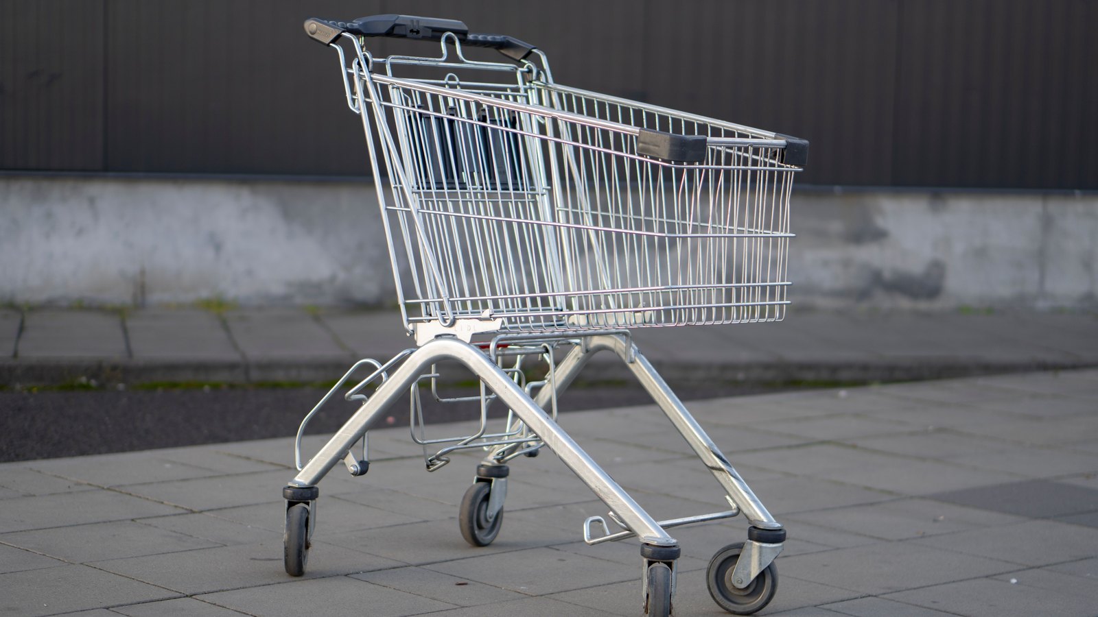 An empty metal shopping cart stands outside a store.