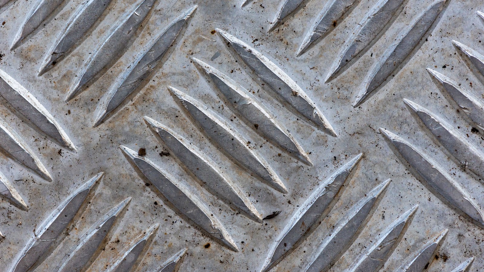 Close view of weathered steel chequer plate, its raised diamond treads worn pale grey and flecked with grit.