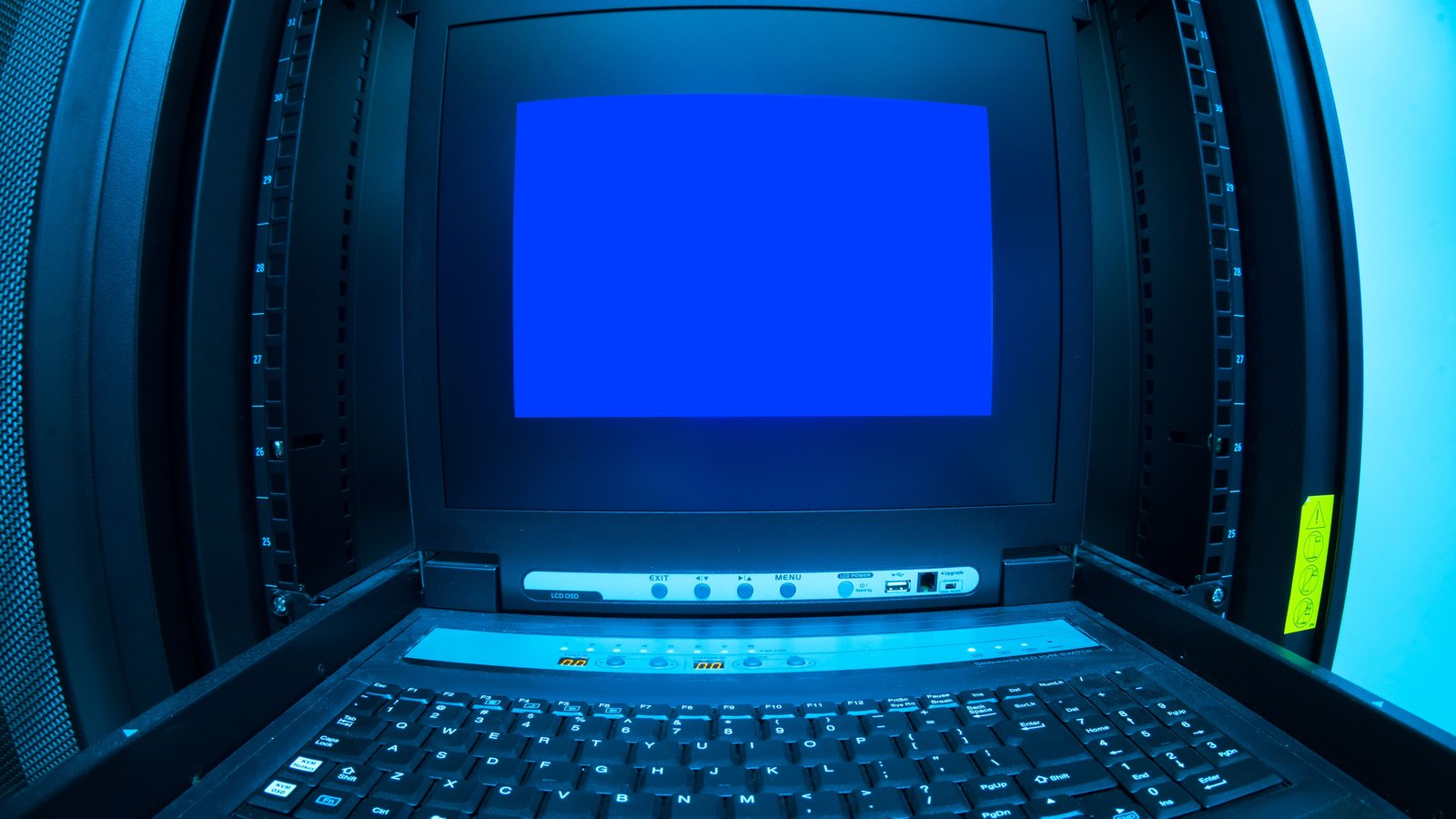 A blank monitor and keyboard mounted inside a blue-lit data center server rack.