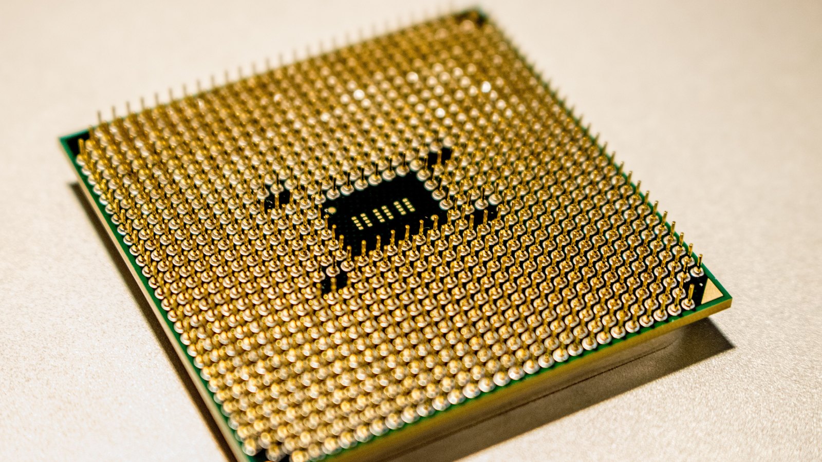 The underside of a packaged microprocessor lying on a pale surface, its dense square grid of gold pins filling most of the frame, with a small dark recess at the centre showing bare solder pads and no markings of any kind.