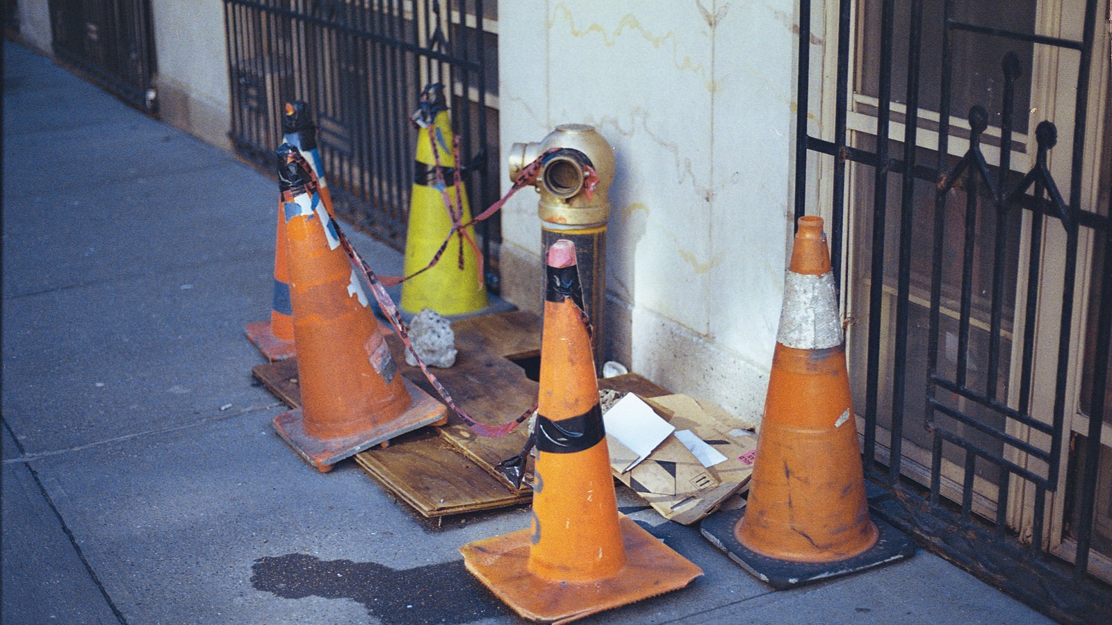 Traffic cones surround a hydrant beside a sidewalk, not a photograph of this sinkhole.