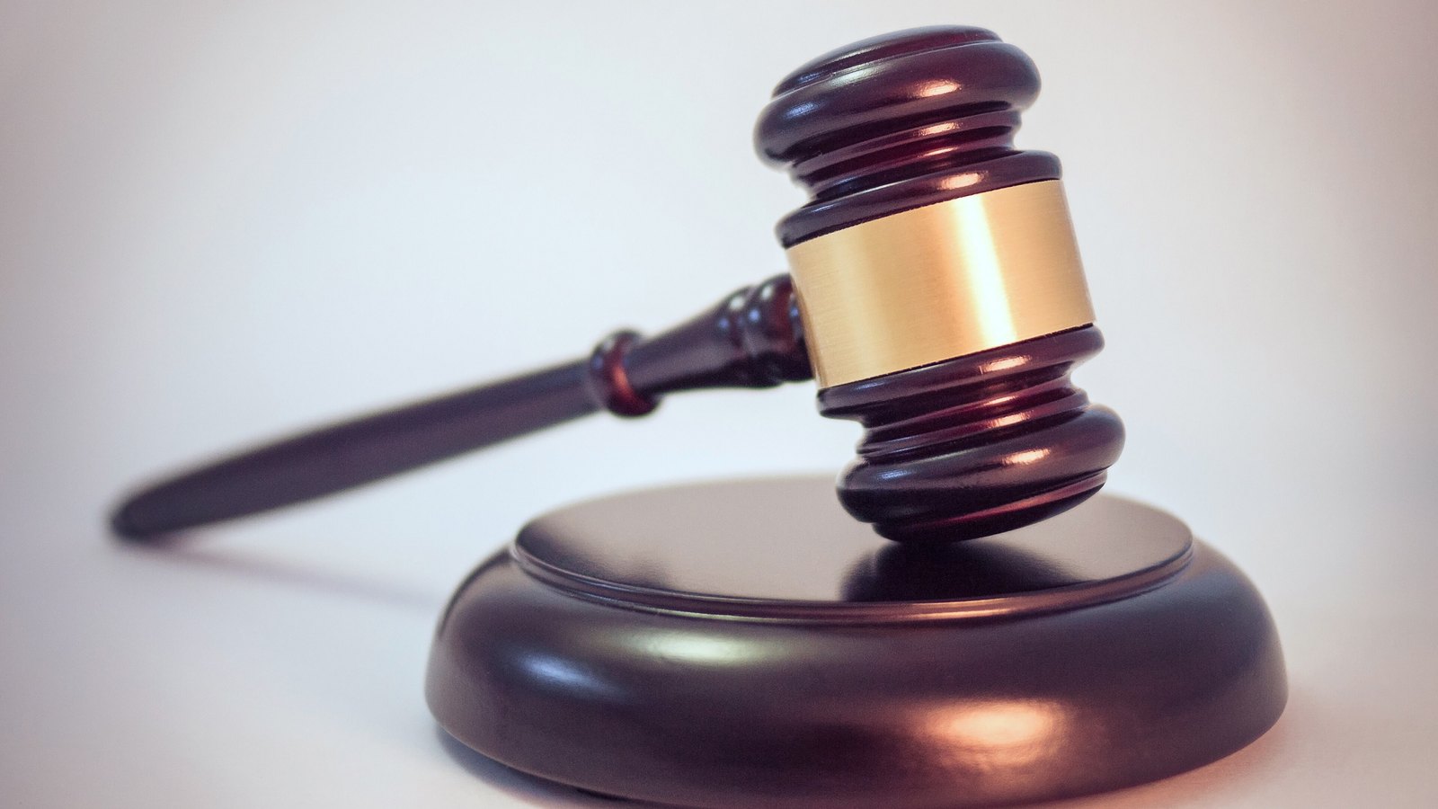 A dark wooden gavel resting above its round block against a plain pale background.