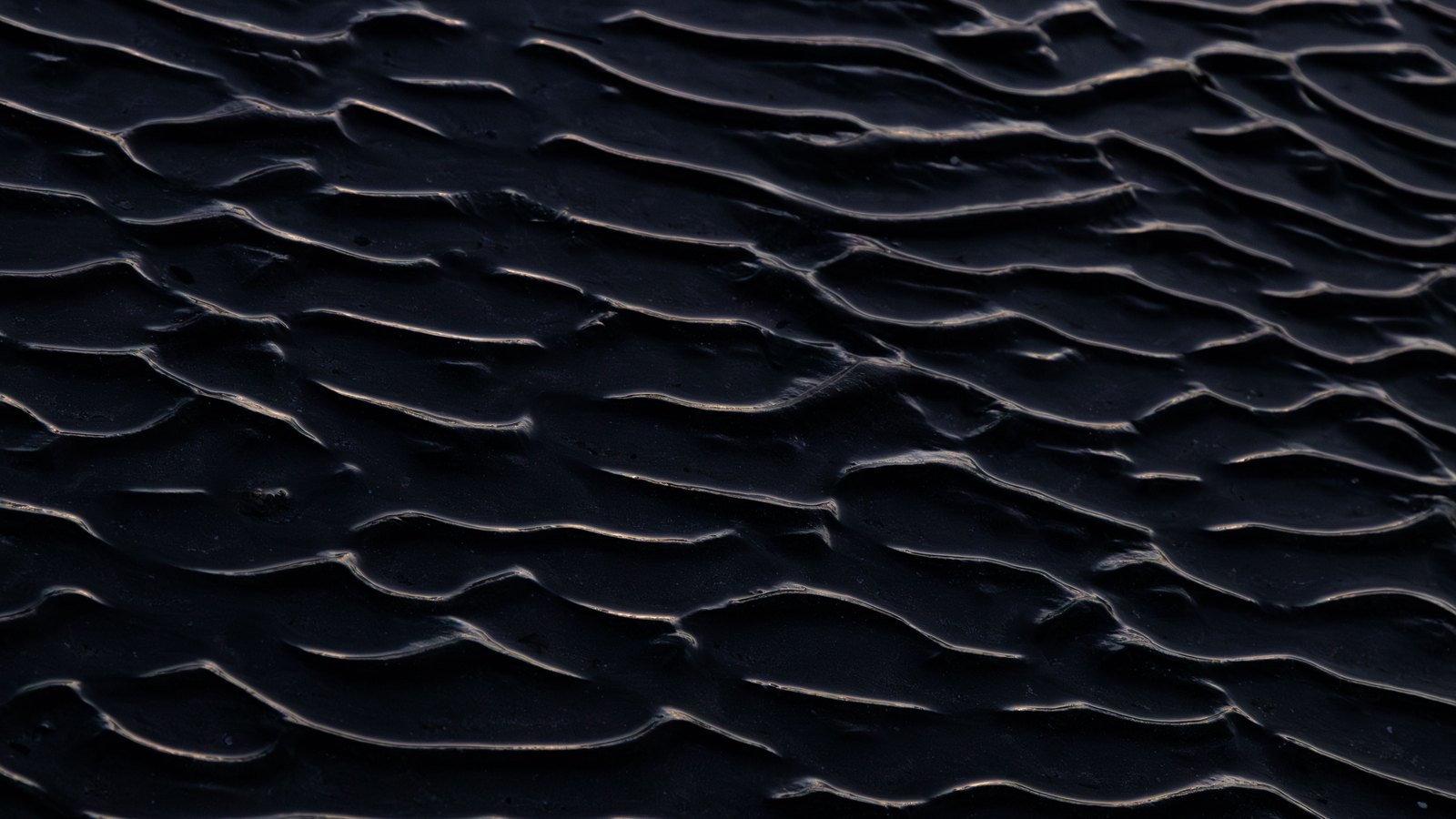 Close ridges of dark sand running in parallel bands across the whole frame, each crest catching a thin line of light.