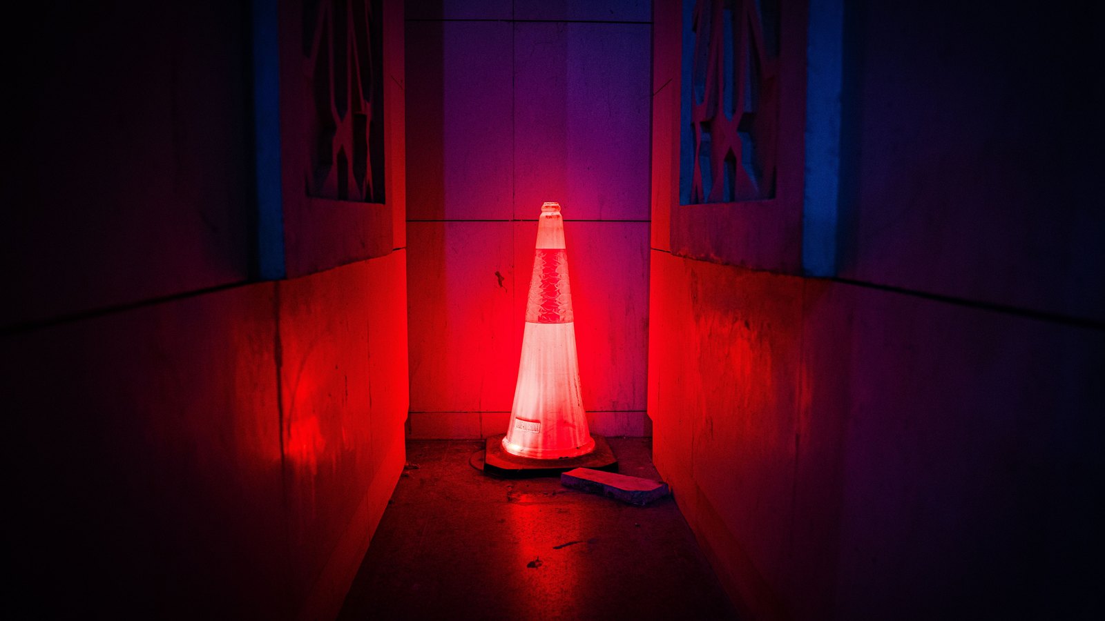 An orange traffic cone illuminated by red and blue warning lights in a dark passage, not a photograph of this event.