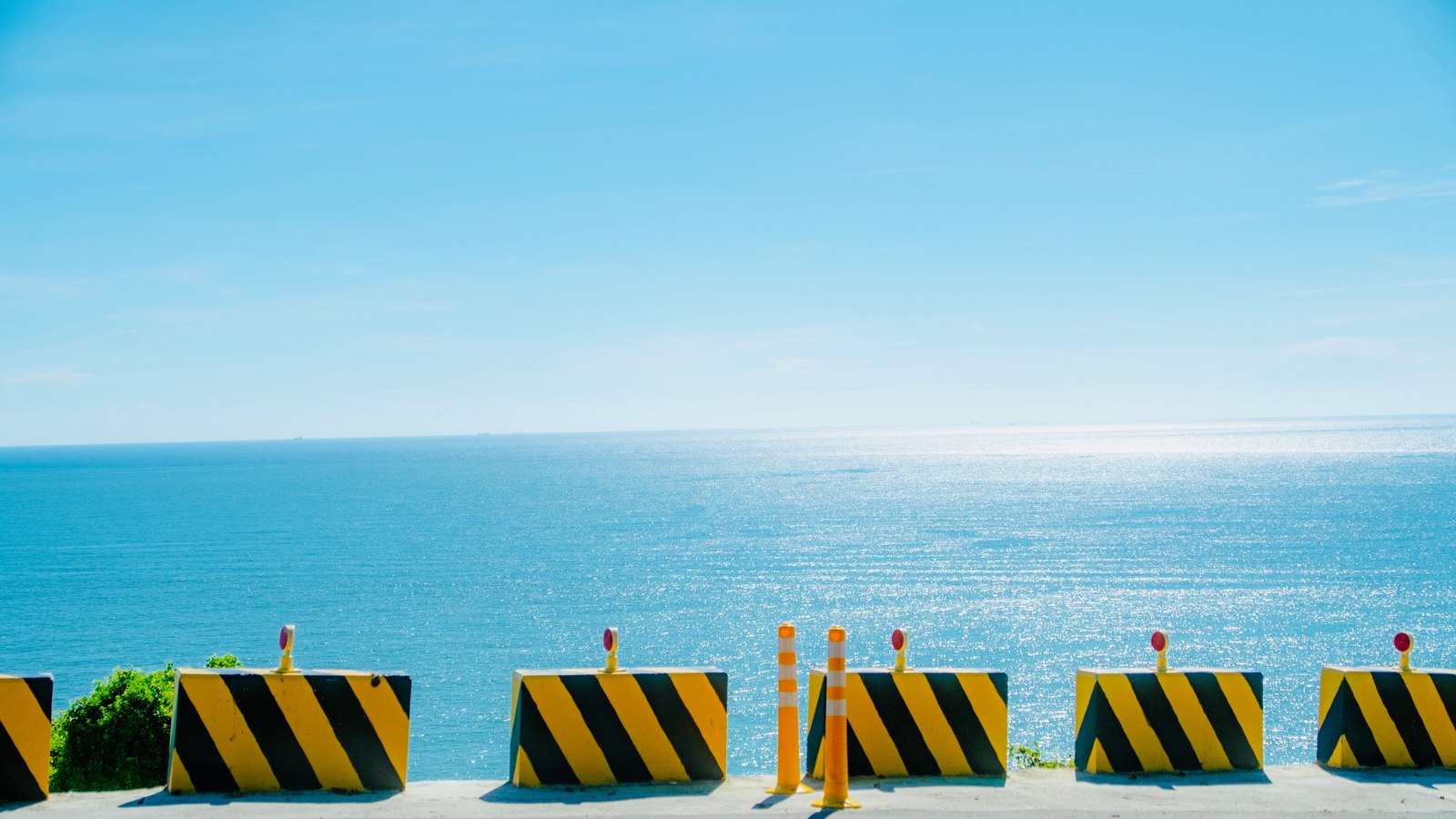 Black and yellow road barriers and orange traffic cones line a coastal roadway, not a photograph of this event.