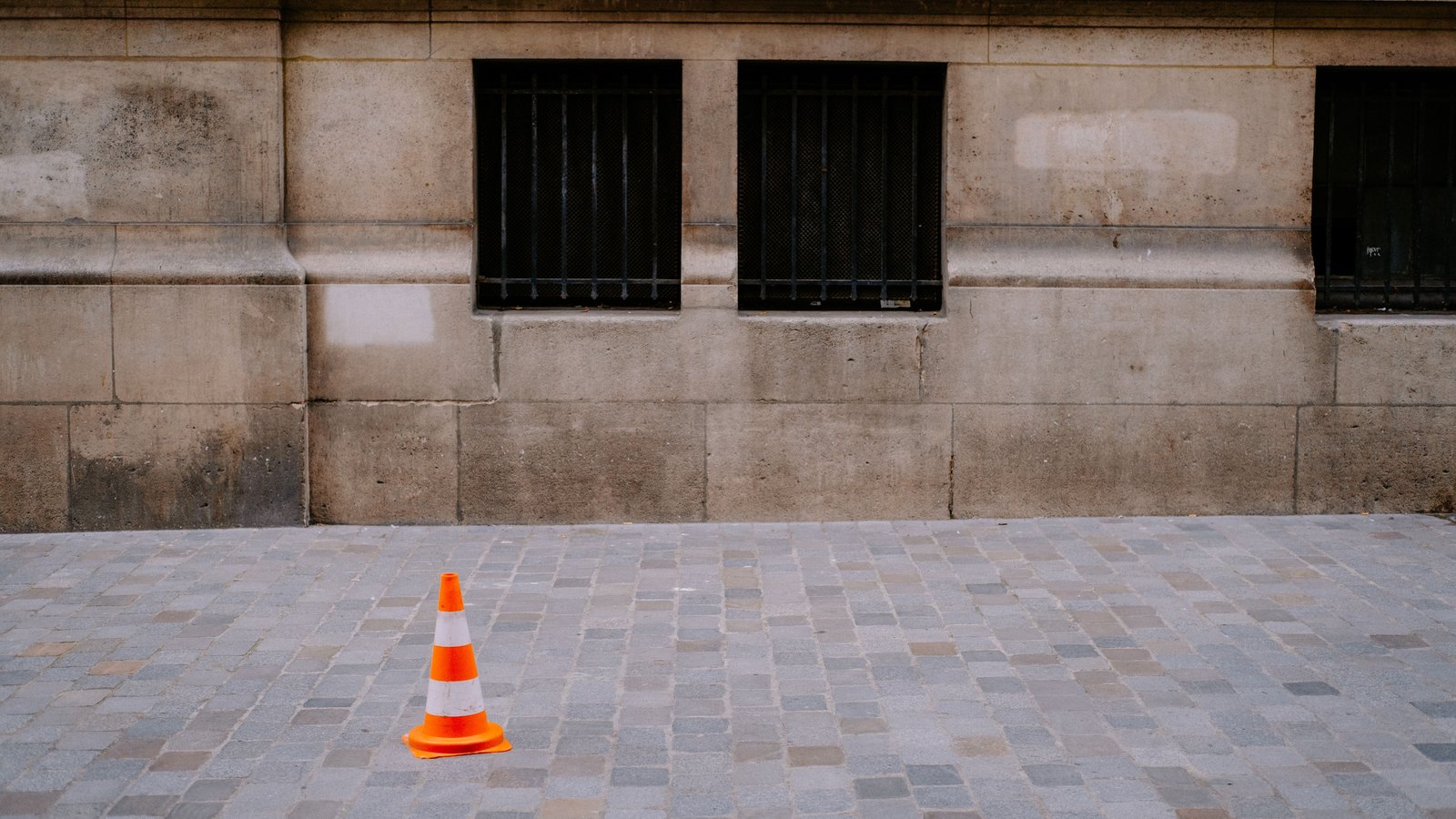 An orange traffic cone stands on paving beside a stone wall, not a photograph of this event.