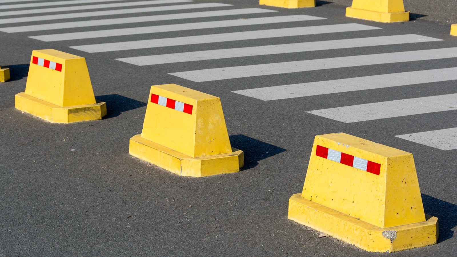 Yellow road barriers line a marked crossing on dark asphalt, not a photograph of this event.