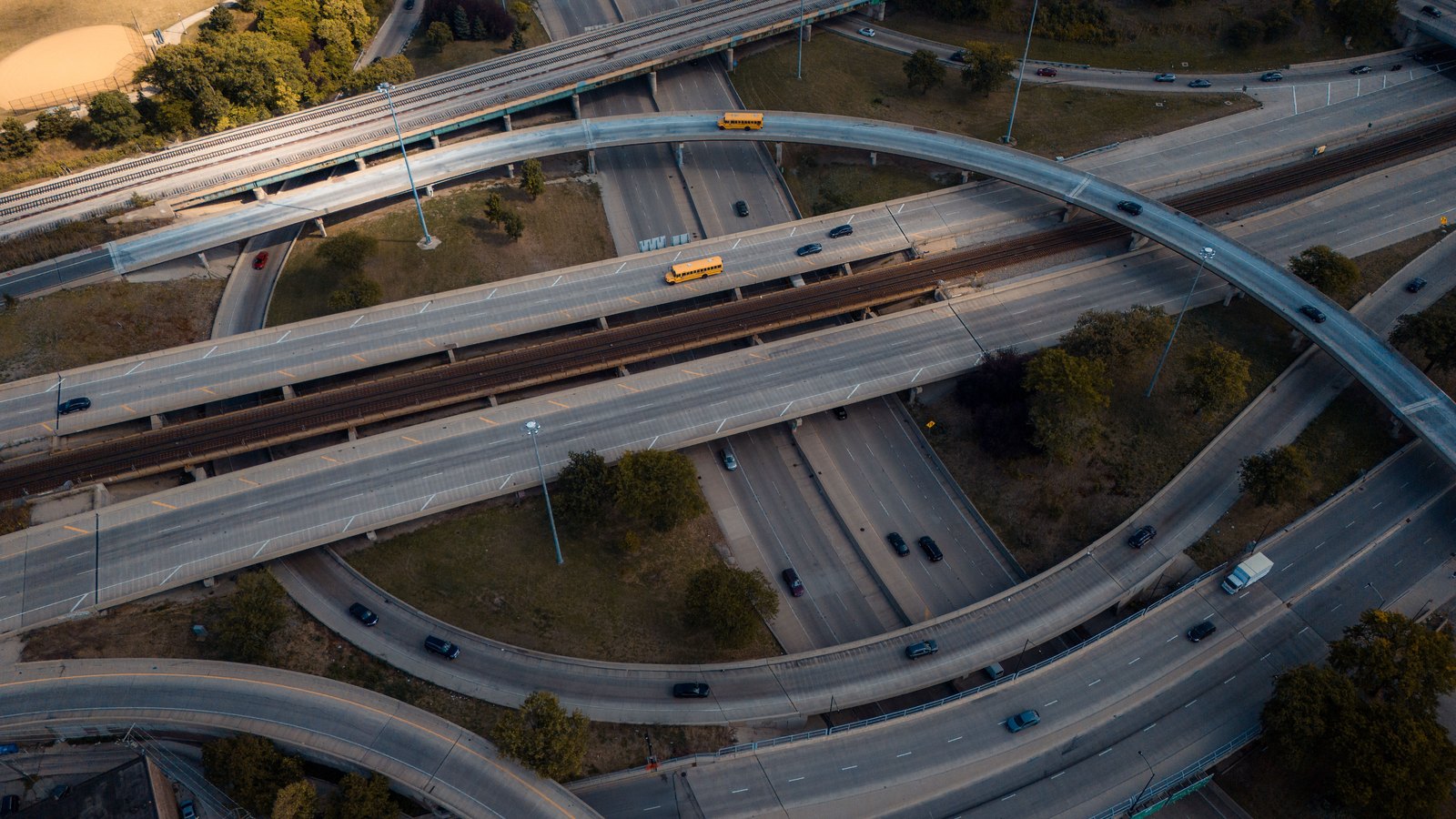 An aerial view of a multi-level highway interchange, with ramps curving over a divided highway and school buses among the traffic.