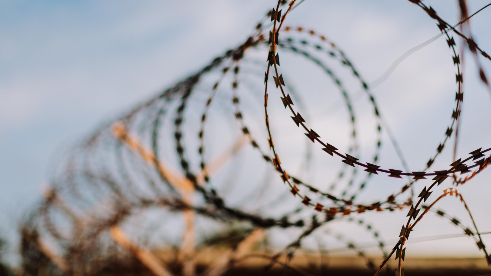 Coils of razor wire running along the top of a fence, photographed close up against a pale overcast sky with the far end of the run falling out of focus, and no people, buildings, vehicles, signs or text in view.