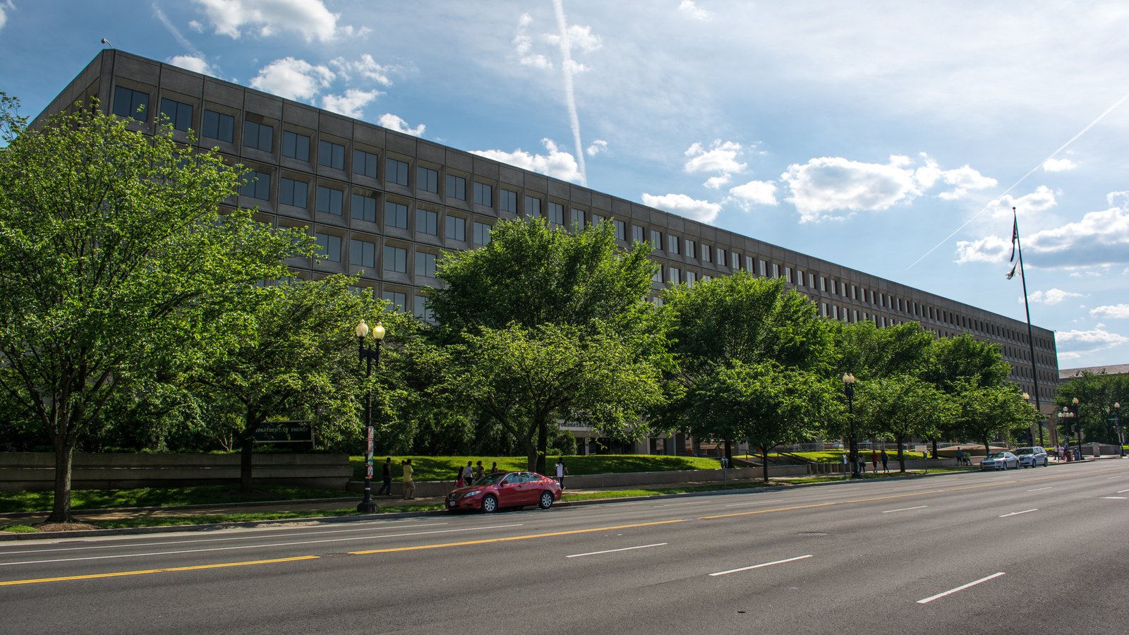 The James V. Forrestal Building on Independence Avenue SW in Washington, seen along its length from street level, a long concrete slab block on square piers with rows of deep-set windows, with street trees and a road in front of it under blue sky.