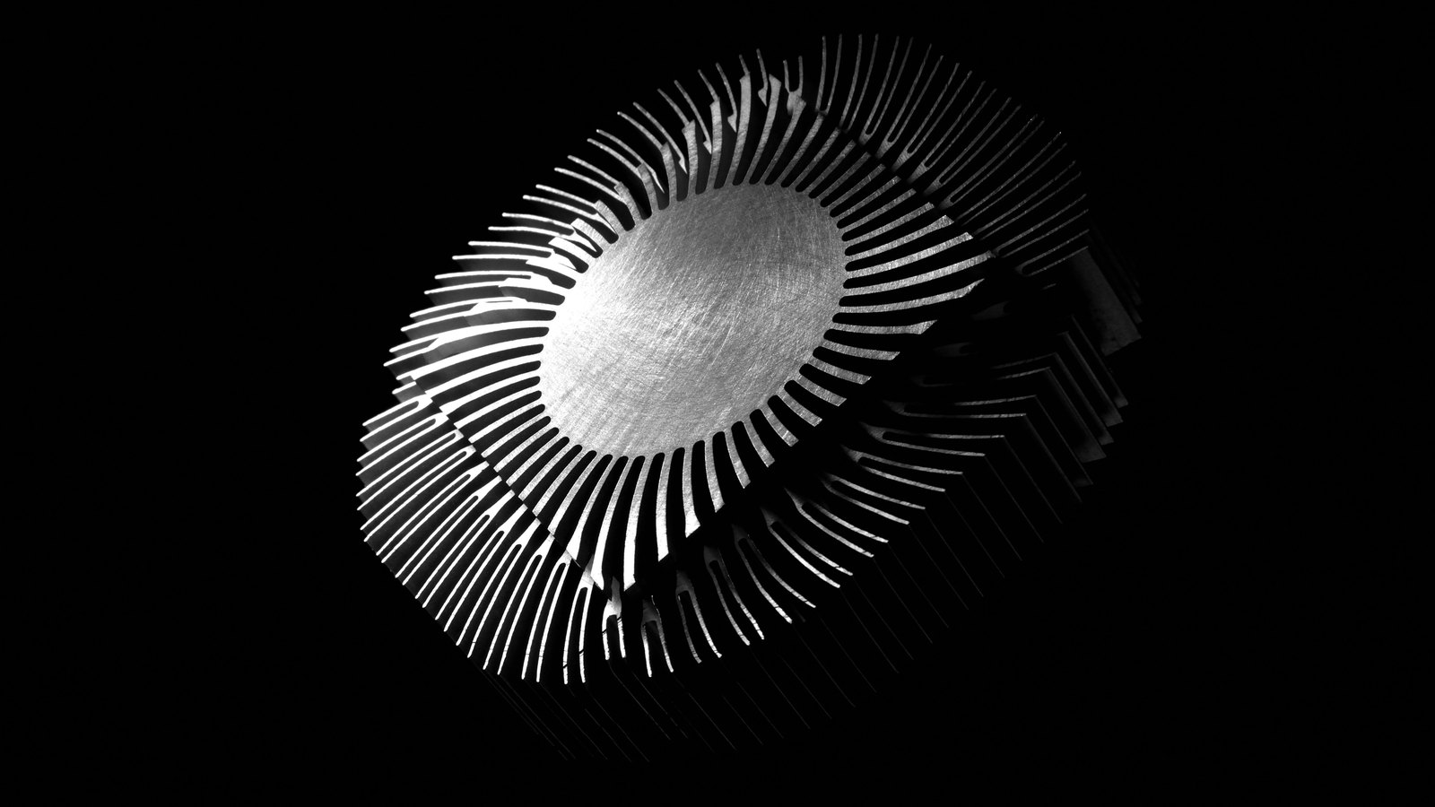 A circular aluminium heat sink lit against a black background, its radial fins fanning out from a brushed metal centre.
