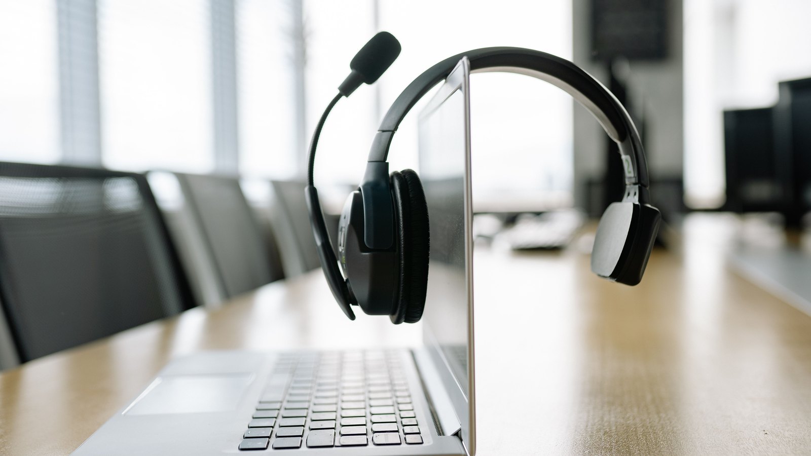 A black communications headset hangs from an open laptop in an empty office, not a photograph of this event.