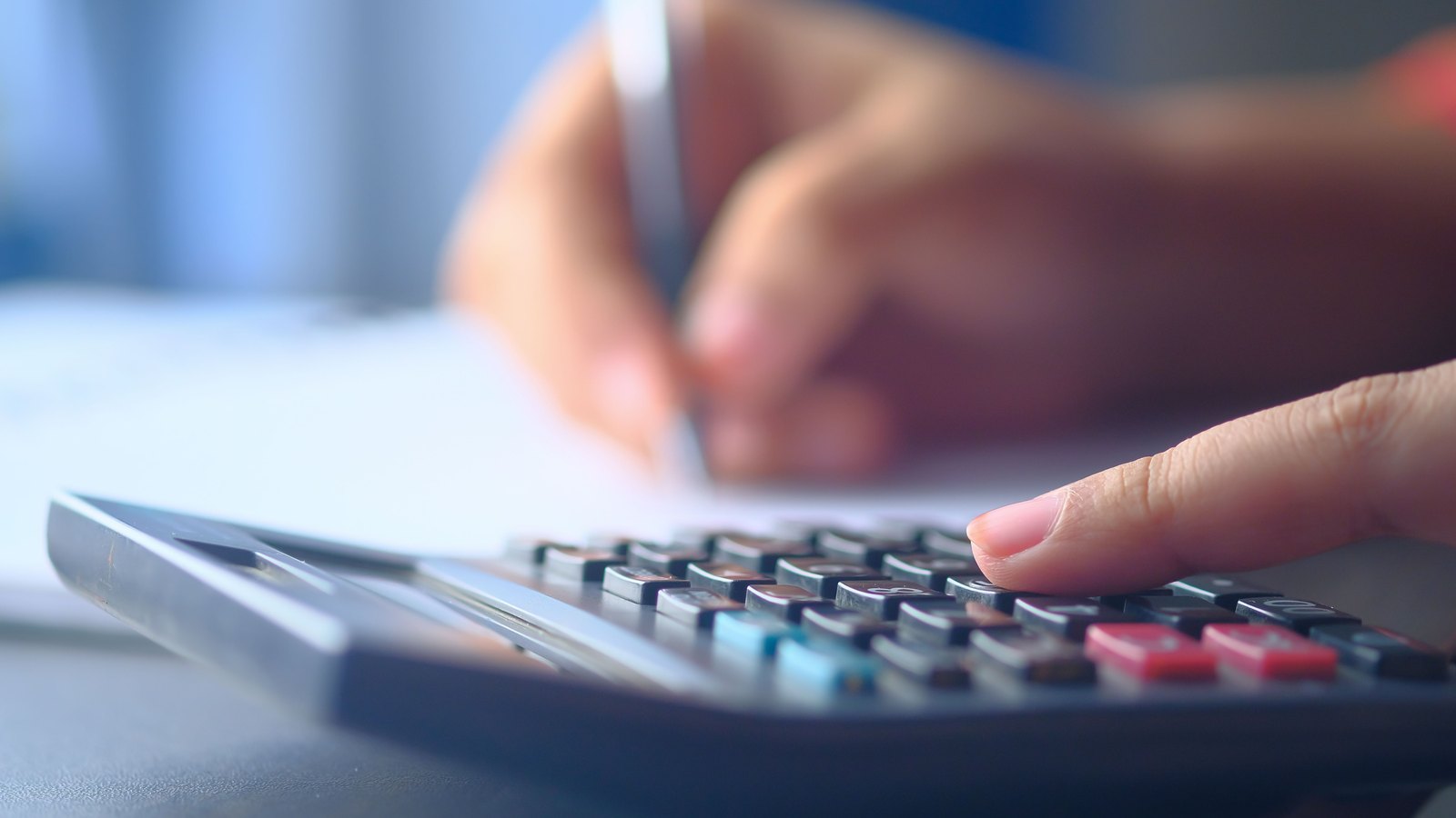 A person enters figures on a calculator beside handwritten notes.