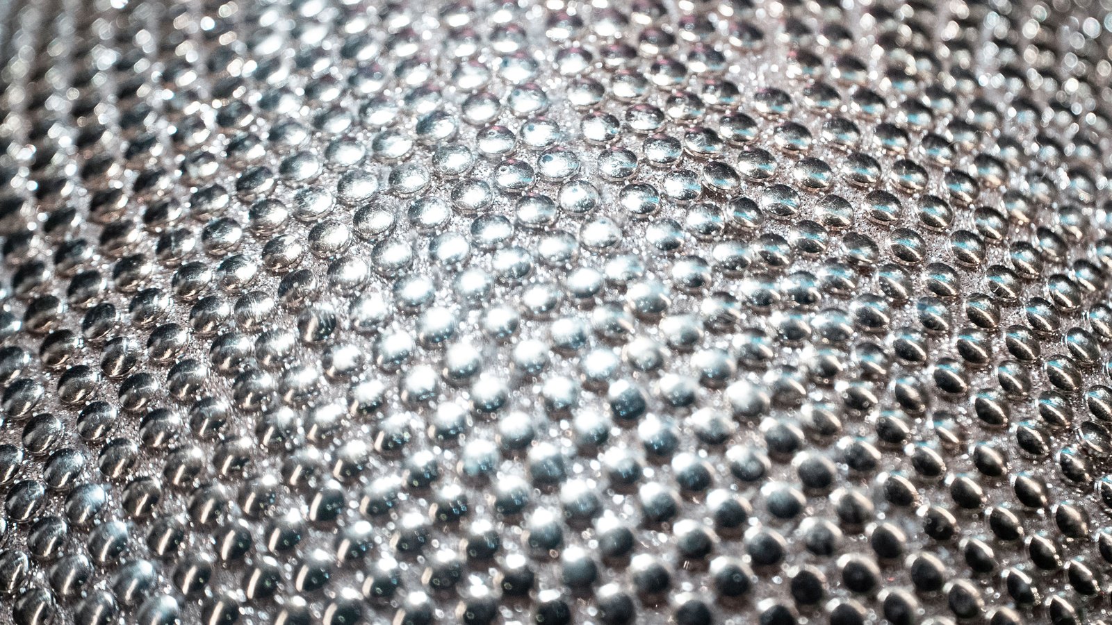 A macro view of a bright dimpled metal sheet, rows of raised round studs catching the light and falling out of focus toward the edges.