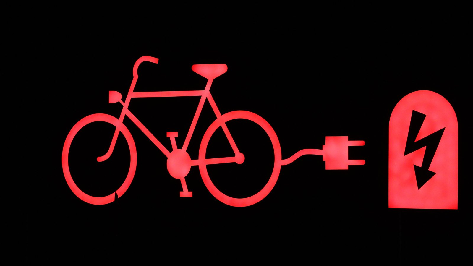 A red illuminated bicycle and charging plug symbol on a black background, a stock image not a photograph of this event.