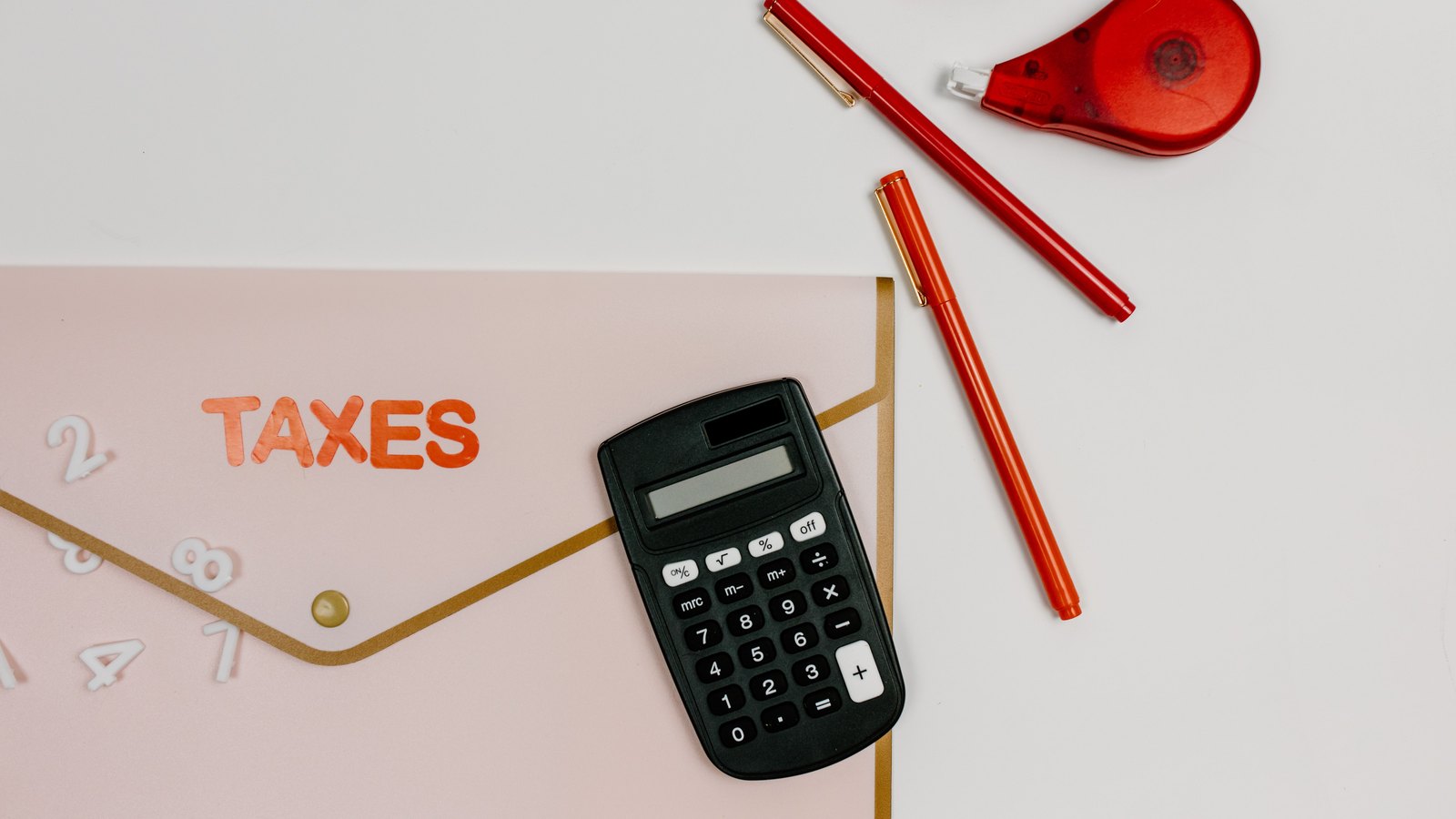 A calculator rests on a folder marked Taxes beside red pens, not a photograph of this event.