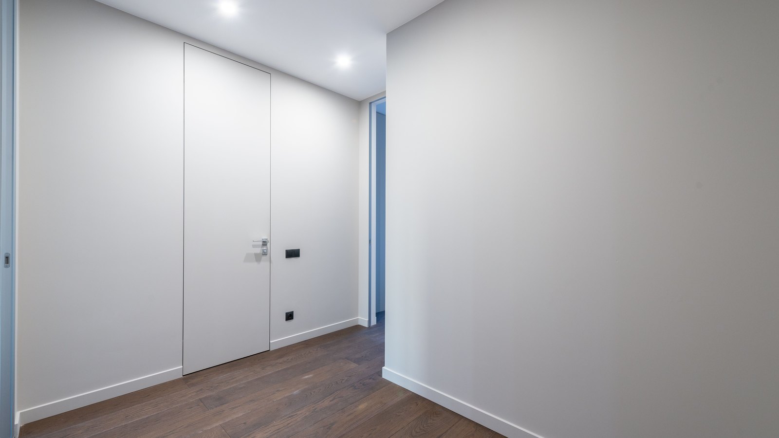 An empty interior corridor with plain white walls, a dark wood floor and a closed flush door standing shut. No people, text, signage, brand mark or identifiable place is visible. A neutral illustration, not a photograph of this case, this defendant, this courthouse or Estero Fire Rescue.