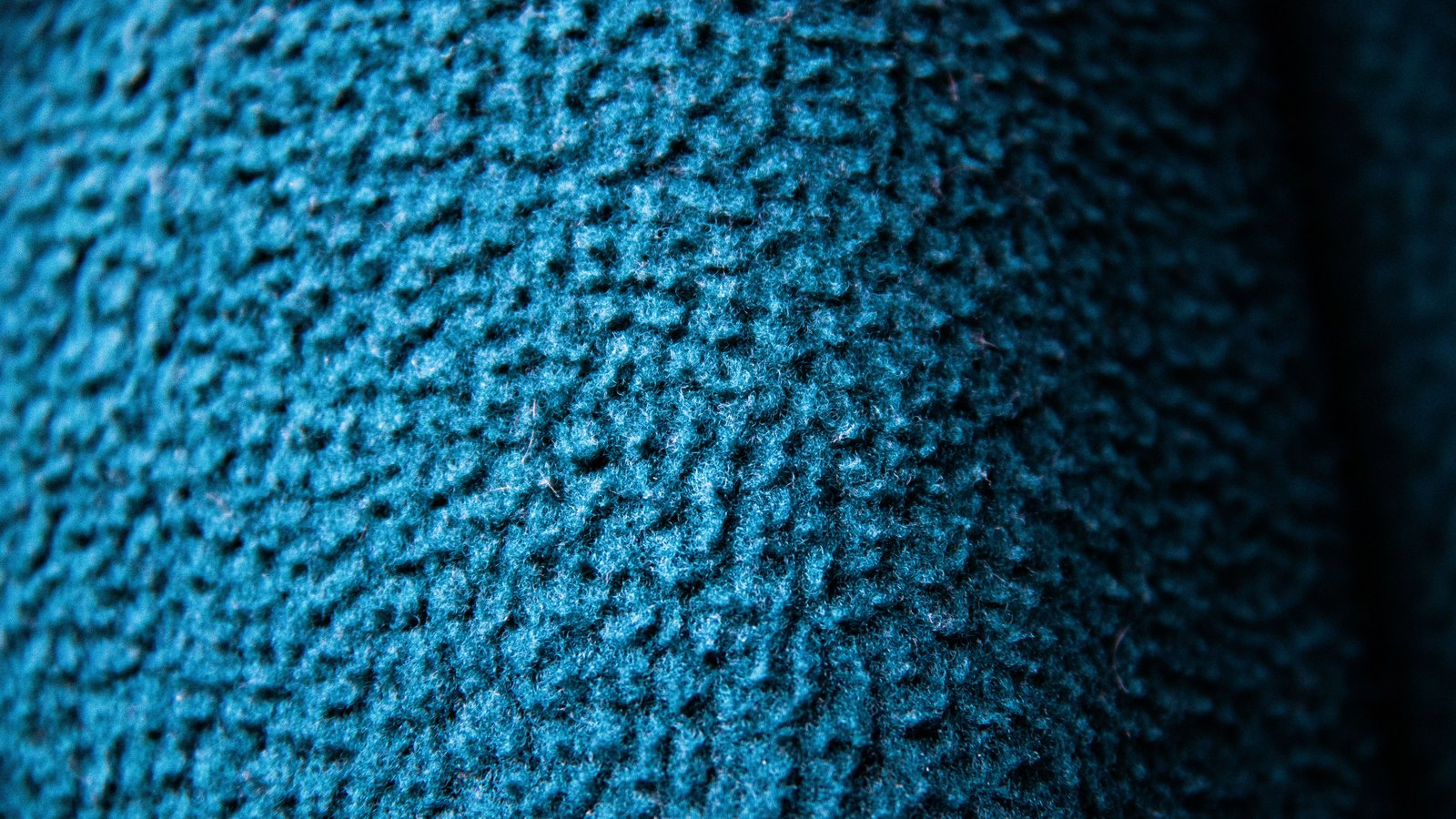 Macro view of dense teal woven cloth, the looped threads filling the frame and falling into shadow at the right edge.