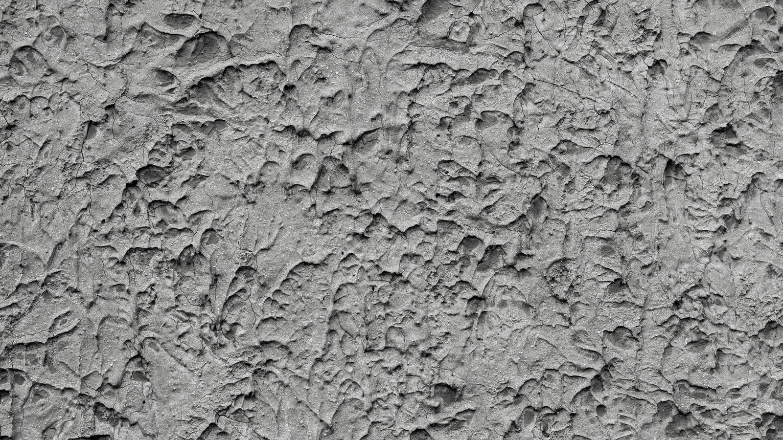 A close photograph of a rough grey cement render surface filling the whole frame, trowelled thickly so the finish breaks into overlapping ridges, shallow pits and fine hairline cracks, with a few pale grains of aggregate showing through. No text, lettering, brand mark, tool, person, vehicle or place is in view.