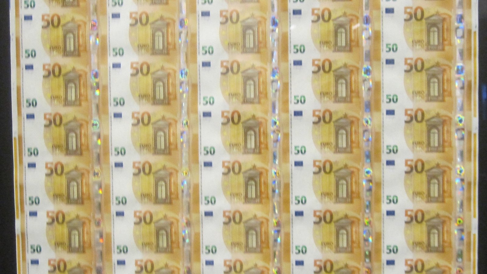 Rows of uncut 50 euro banknotes still joined edge to edge on a printed sheet, the orange notes repeating in five columns with holographic strips running between them. No person or brand is in frame.