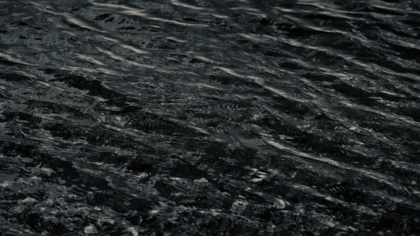 A black and white close-up of open water, its surface broken into small overlapping ripples, with no horizon, shoreline or vessel in the frame.